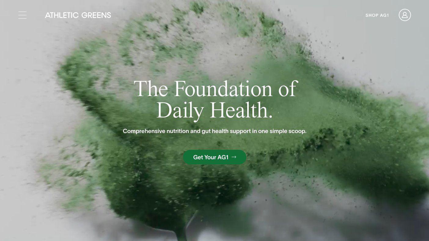 An explosion of green AG1 powder, a still from a video. Foreground text reads 'The foundation of daily health'.