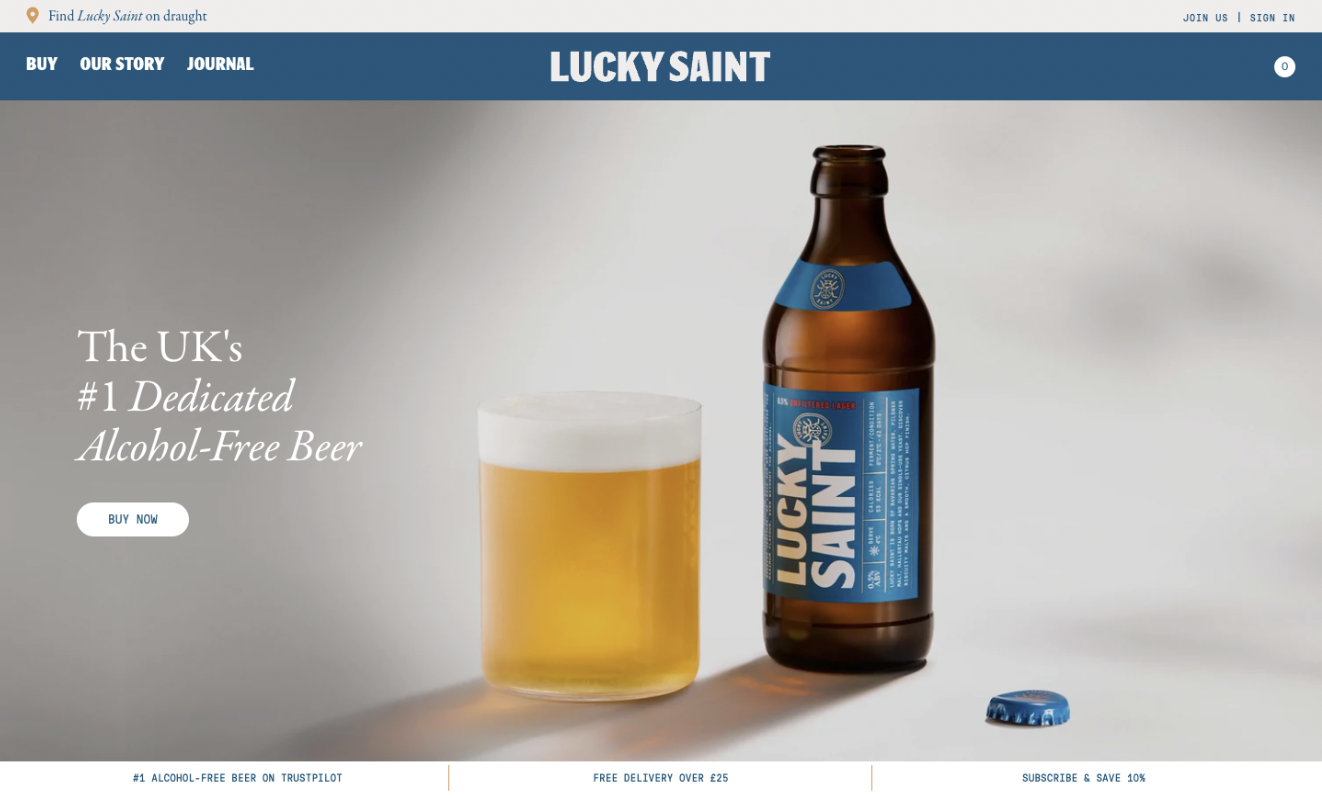 Blue navigation menu across the top with large hero image that fills the screen below. Image shows an empty bottle of Lucky Saint lager next to a full glass of beer. Text on image states this is the UK's #1 alcohol-free beer.